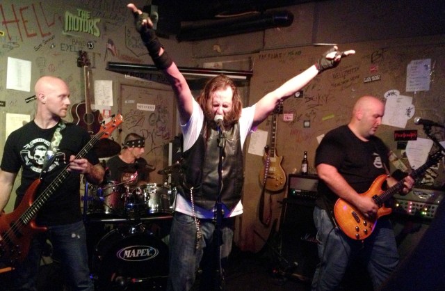 Lead singer Ralph Dunn throws up his hands during The Devil and the Southern Fellowship's set at Cafe Acoustic in St. Joseph, Missouri on 9/13/13. Left to right; Sean Selecman on bass, Danny Gray on drums, Ralph Dunn at the mic and Chad O'Callaghan on lead guitar; guitarist Sean Sollars is out of frame to stage left.