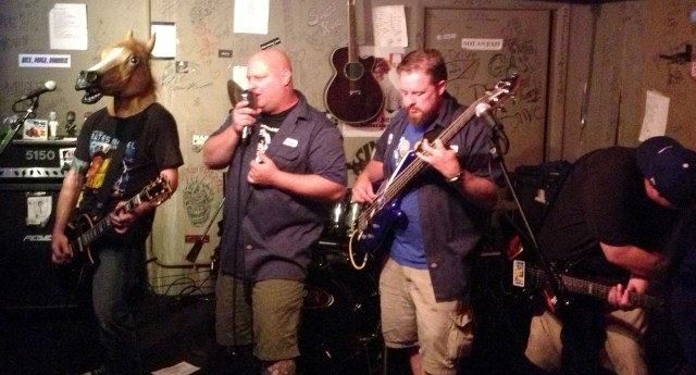 IT brings cinema to the small stage at Cafe Acoustic in St. Joseph, Missouri on 9/13/13. Left to right: Todd Cooper wearing a horse head and playing guitar, Rick Hoffman on vocals, Will Stuck on bass and Ric Howard on guitar; obscured from view is drummer Dan Thompson. 